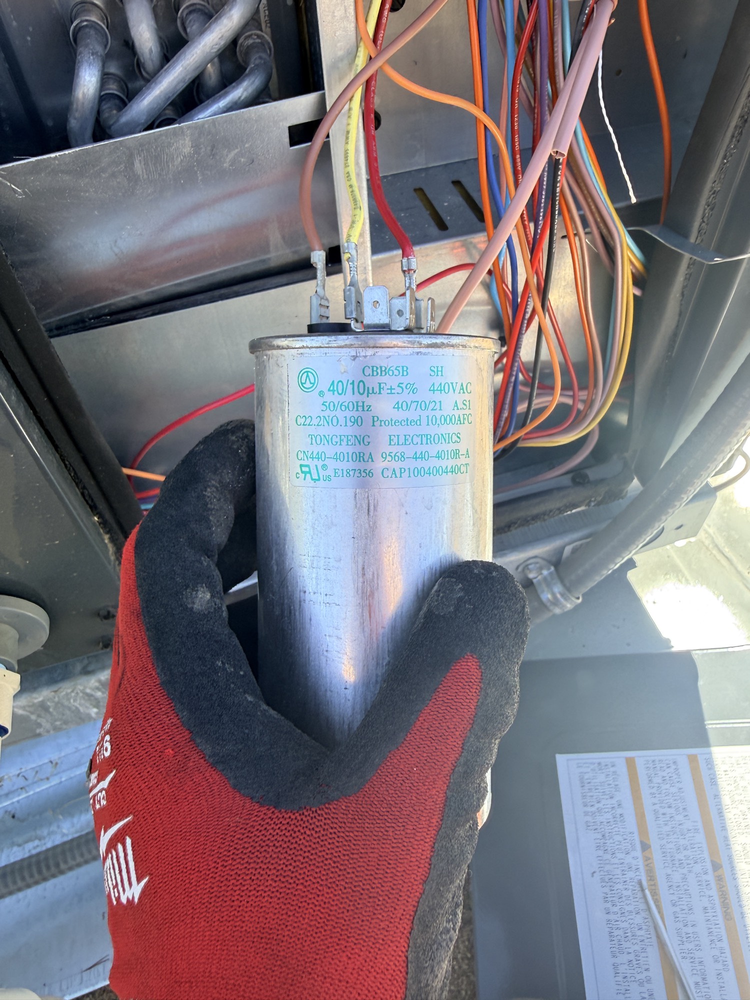 Dual run capacitor, 40/10 microfarad at 440 volts, held in a work glove with the condenser panel open